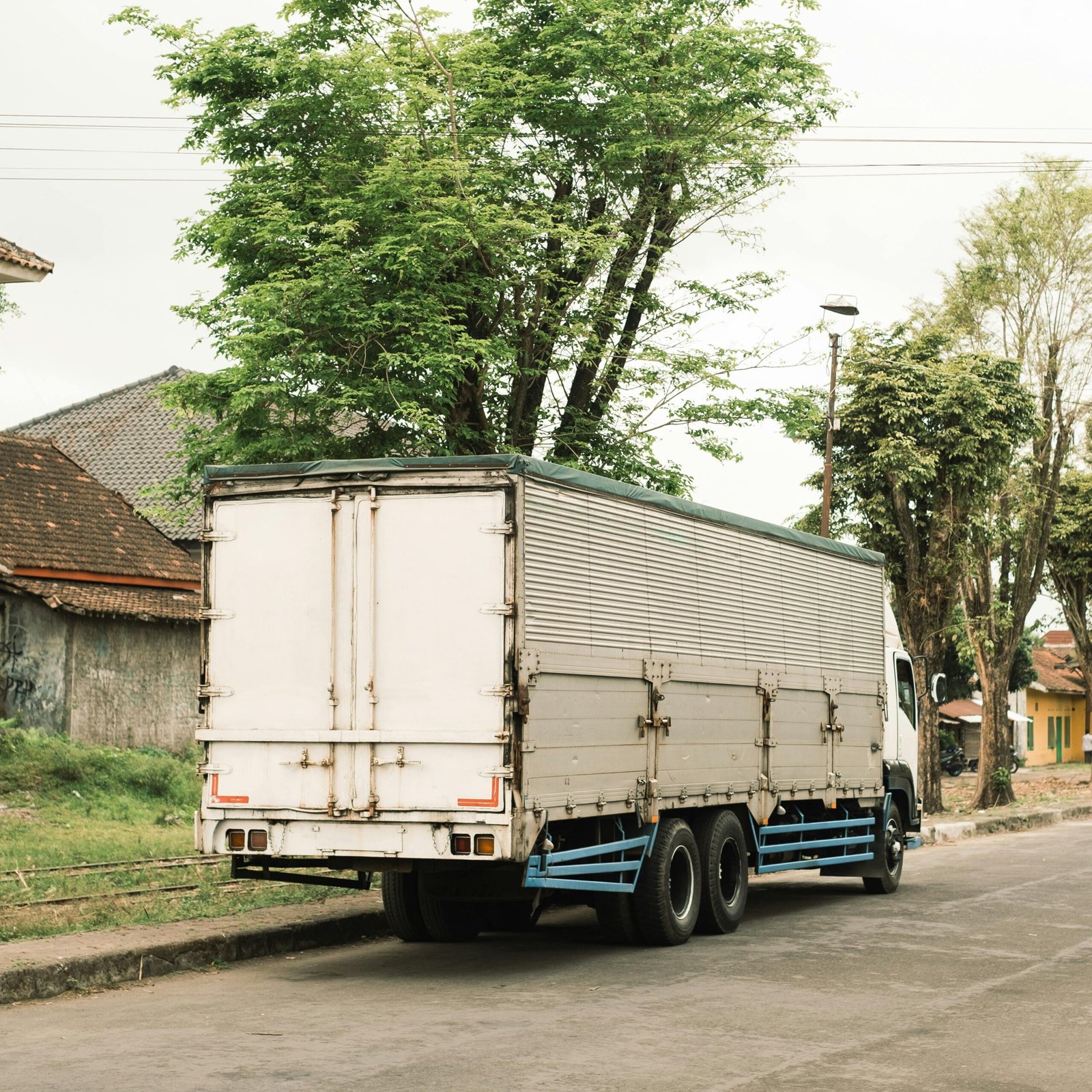 A heavy-duty cargo truck parked on a city street surrounded by lush greenery and buildings.